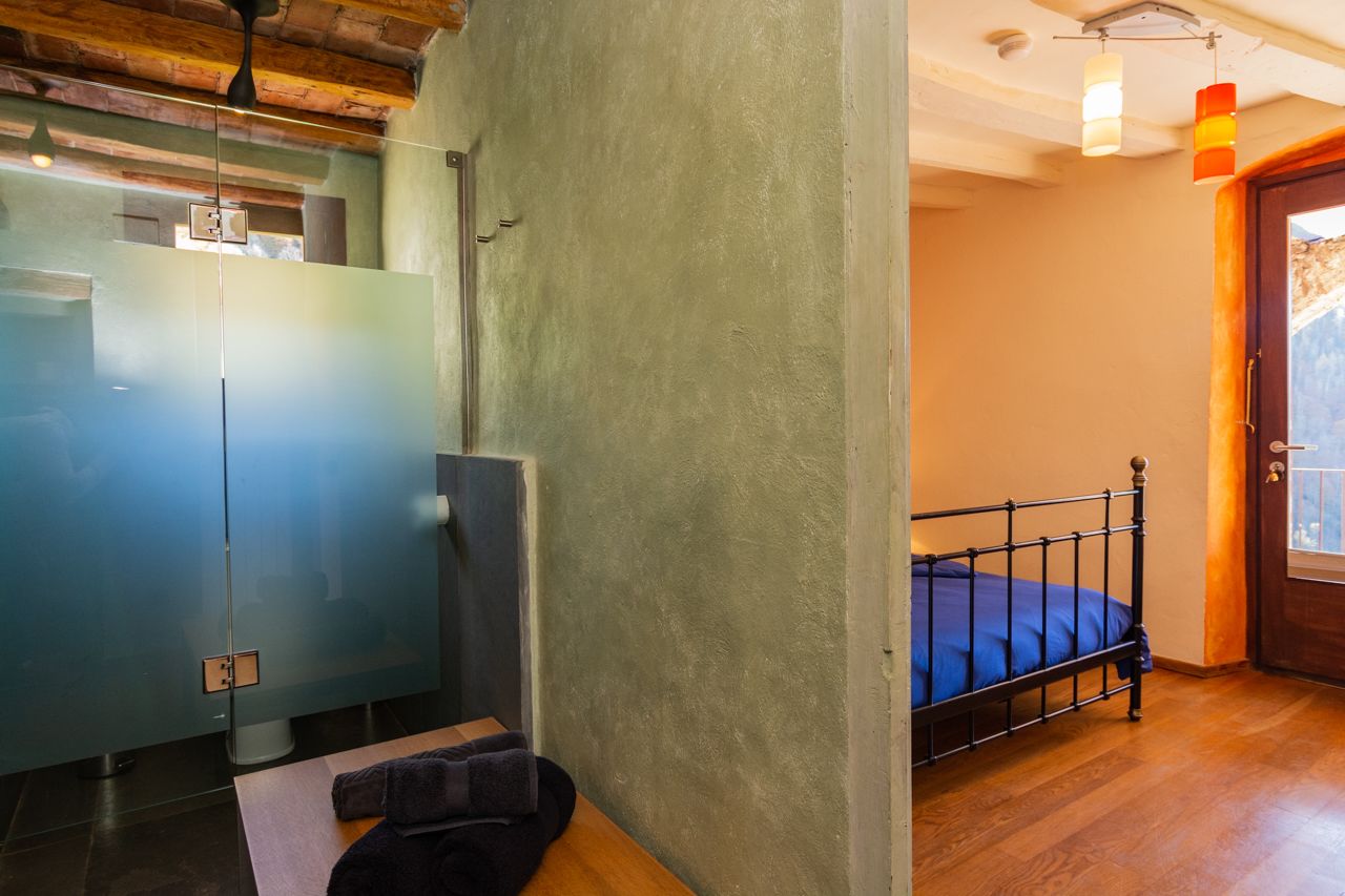 A bedroom with a bed, a wooden floor, a door with a view, and a glass partition.