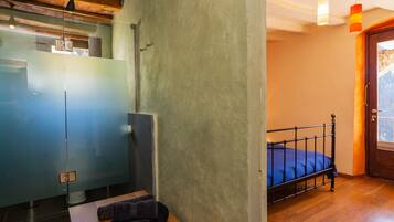 A bedroom with a bed, a wooden floor, a door with a view, and a glass partition.