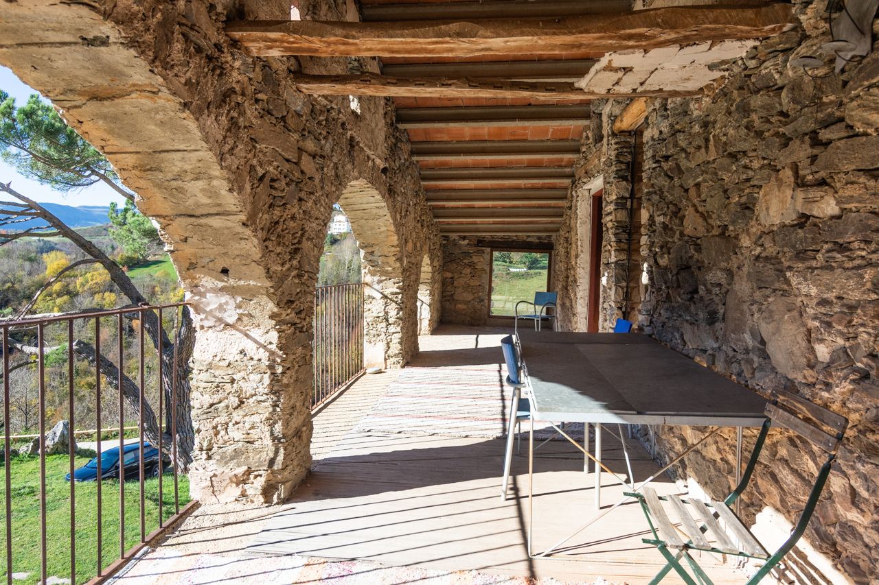 Un patio al aire libre con paredes de piedra, techo de madera, una mesa y sillas.