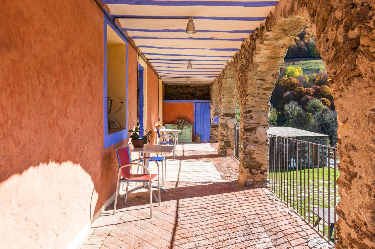 Une terrasse extérieure couverte, avec une table et des chaises, une porte bleue et une vue sur un paysage rocheux.