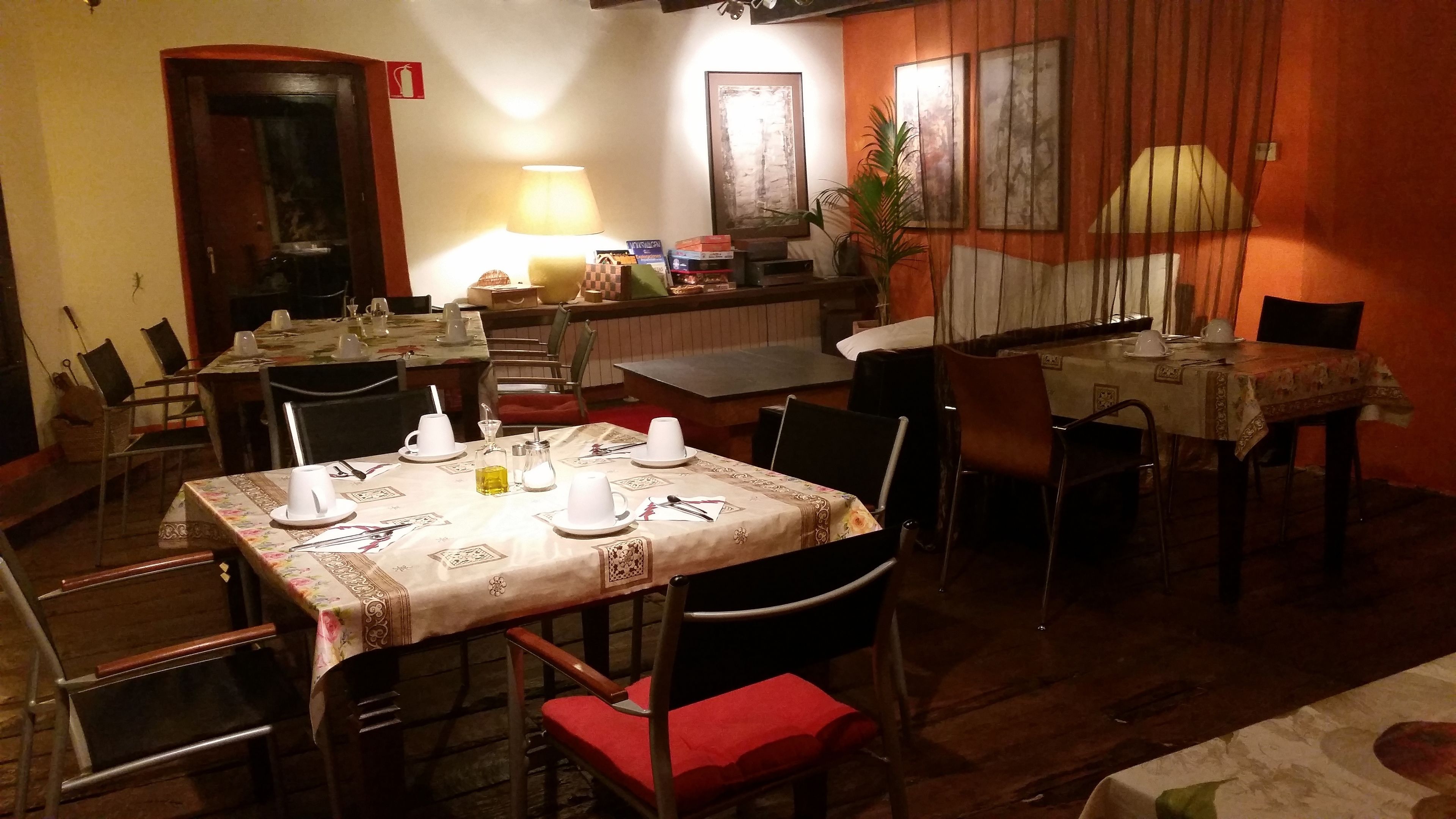 A dining area with tables set for four, chairs, a lamp, and artwork on the walls.