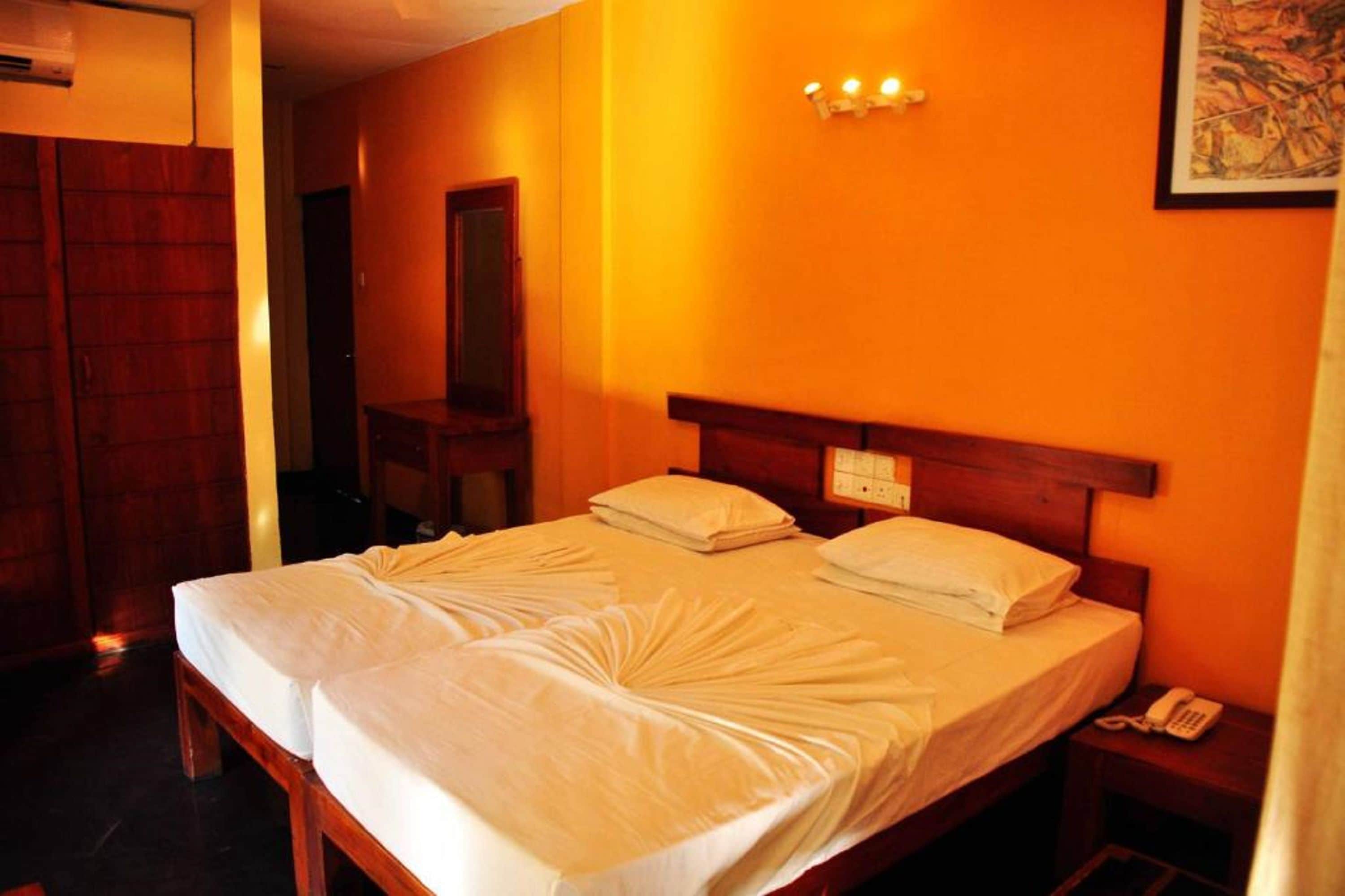 Une chambre d’hôtel avec deux lits, une tête de lit en bois, un téléphone sur la table de chevet et un luminaire fixé au mur.