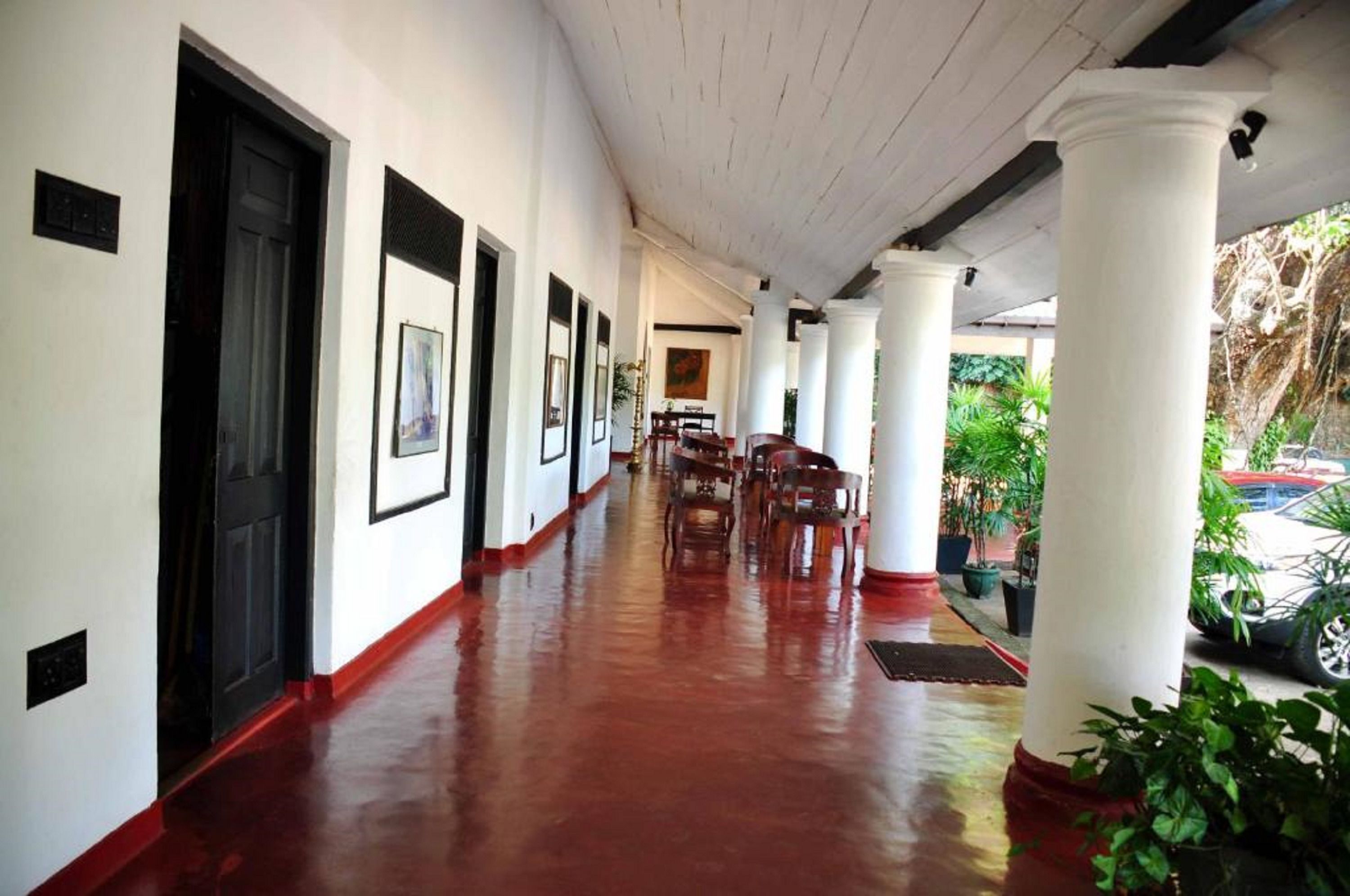 A corridor with white columns, framed pictures on the walls, and a red floor.