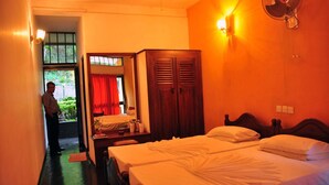 A hotel room with two beds, a wardrobe, a mirror, and a window with red curtains.