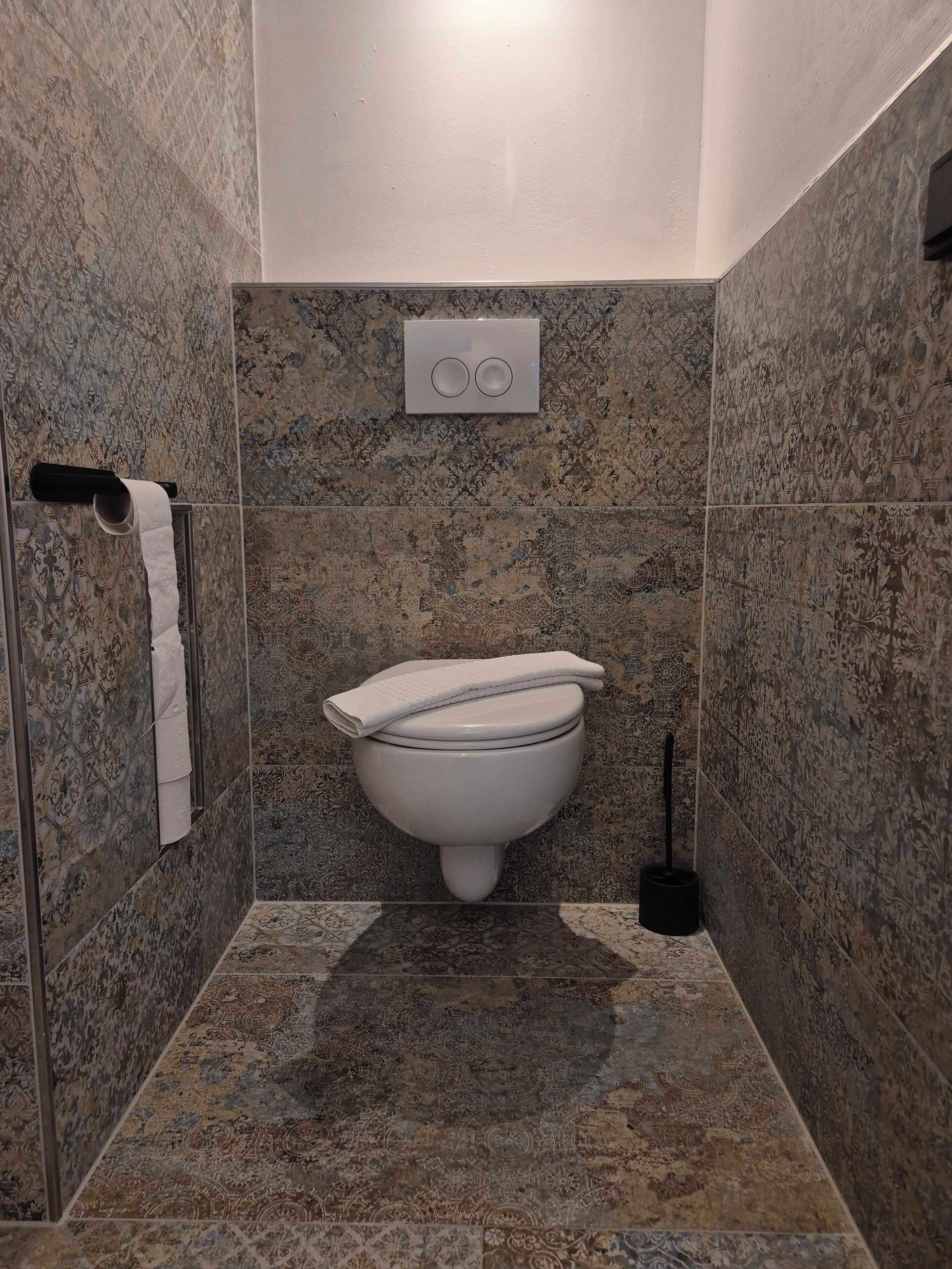 Un baño con inodoro, dispensador de toallas y cepillo para inodoro.