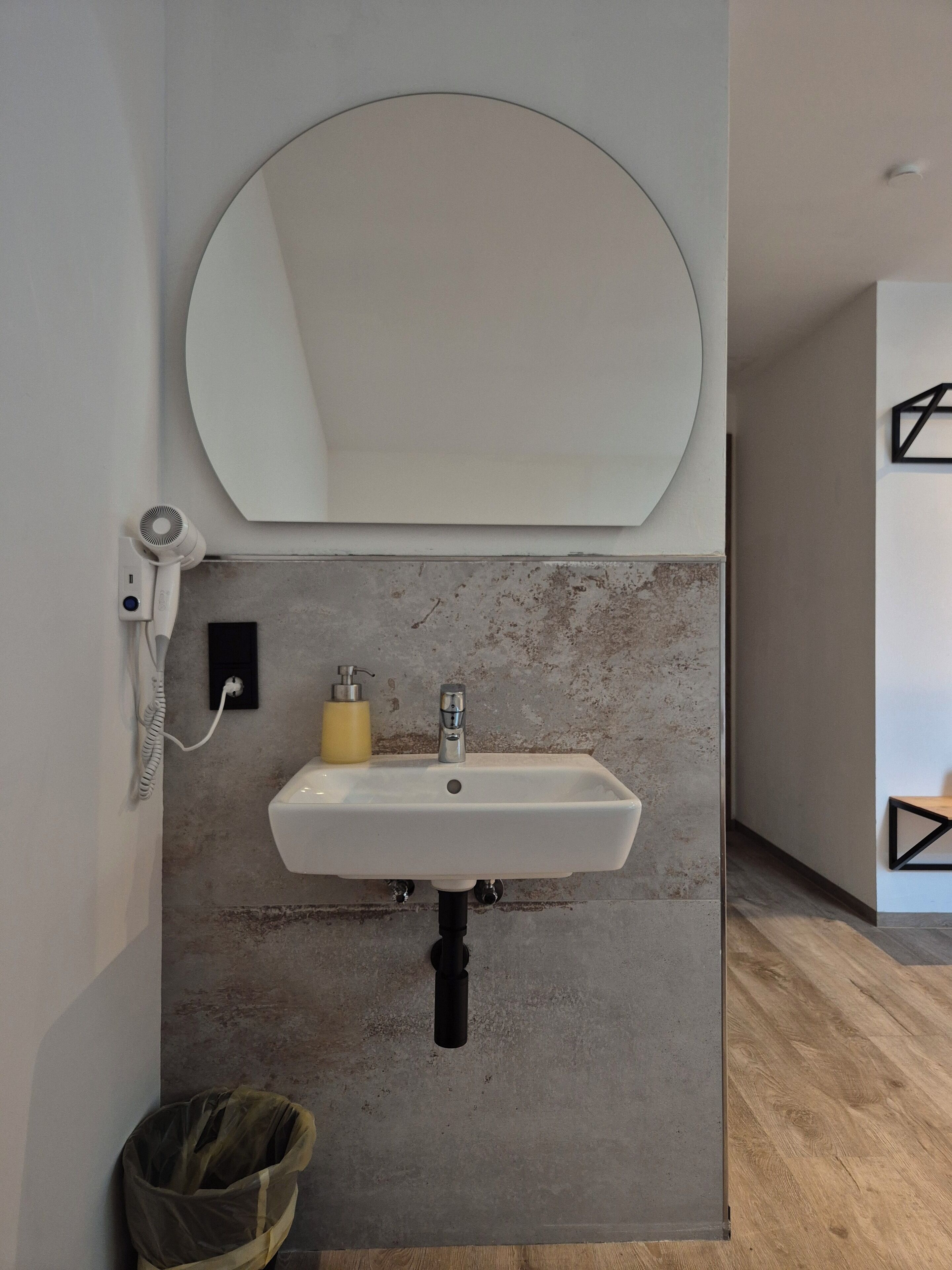 A bathroom with a white sink, a round mirror, a yellow soap dispenser, and a hairdryer on the wall.