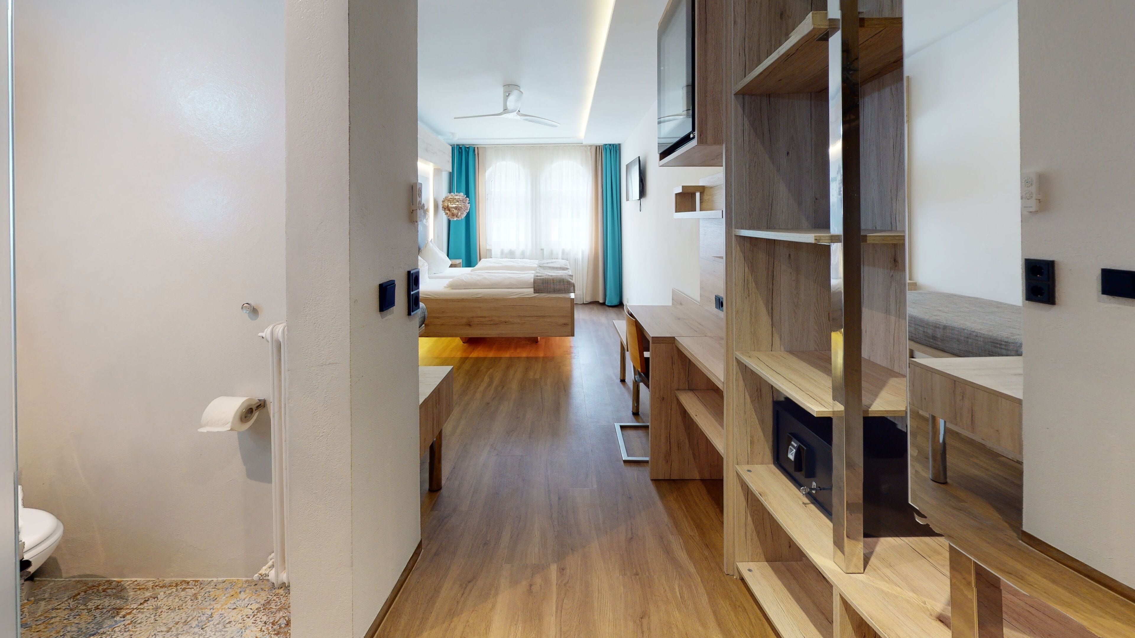 Una habitación de hotel moderna con piso de madera, una cama con cabecera, un escritorio con silla y un armario.