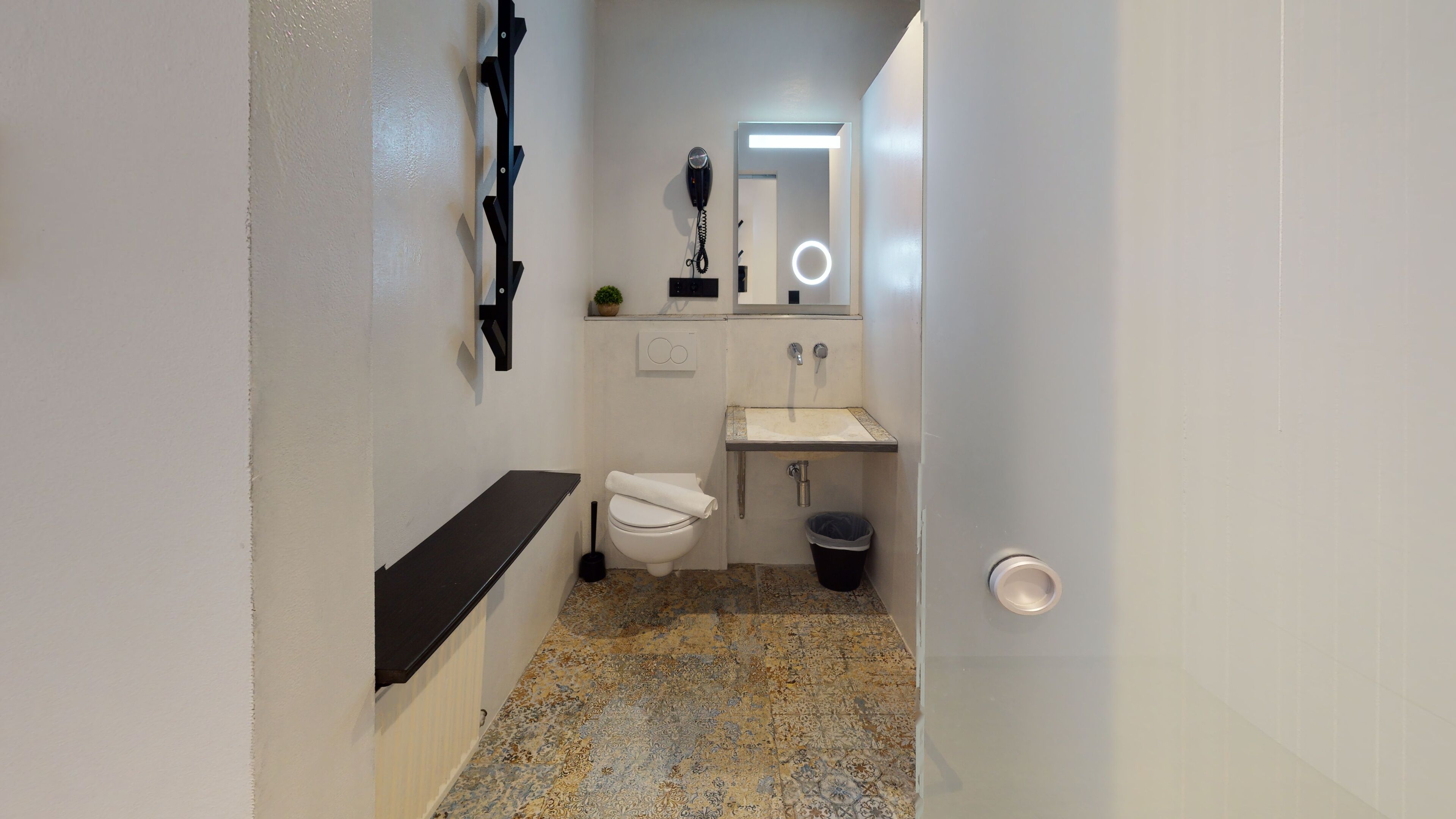 A narrow bathroom with a toilet, sink, and hairdryer mounted on the wall.