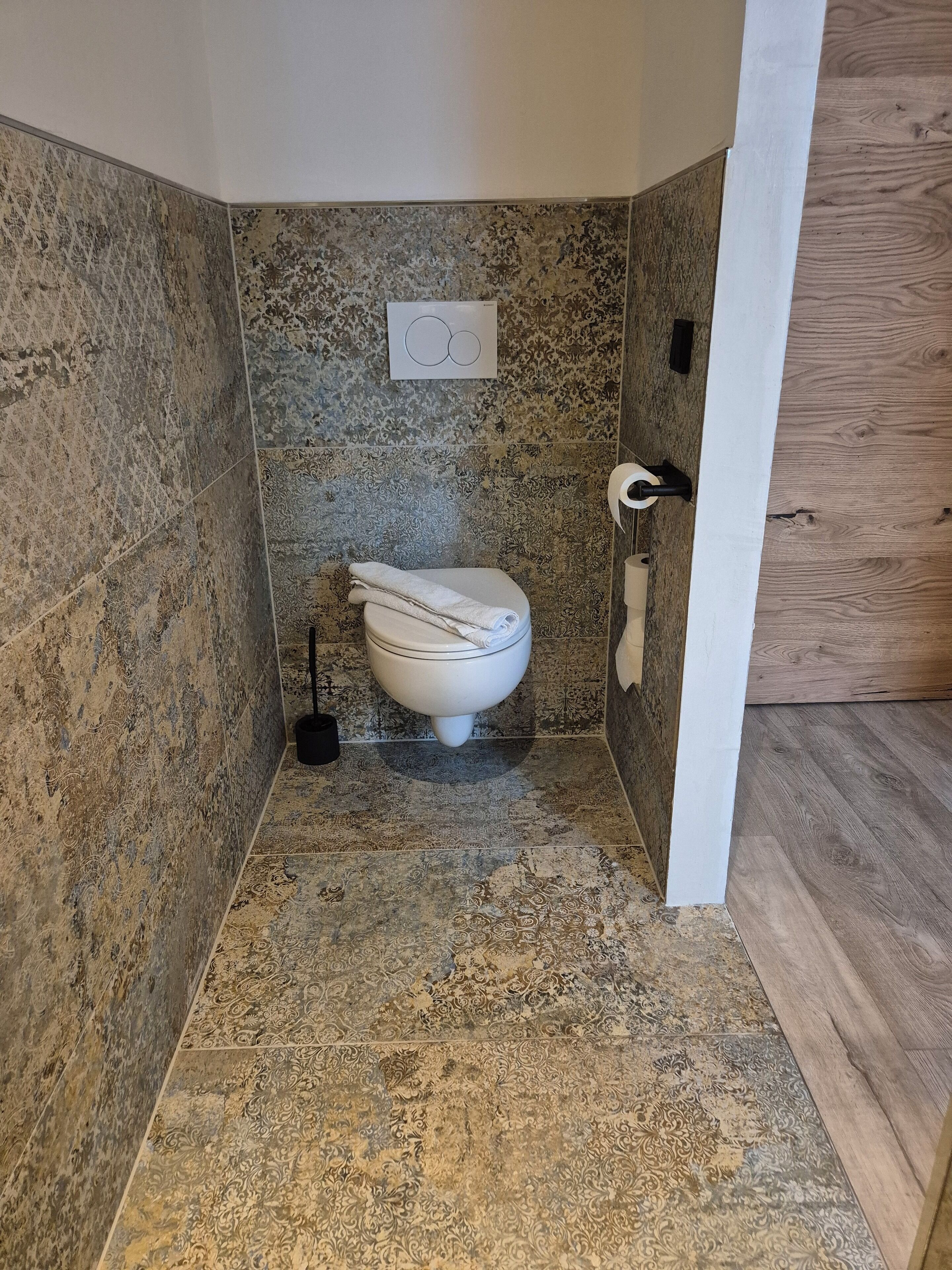 A bathroom with patterned tiles, a toilet, a bidet, and a toilet paper holder.