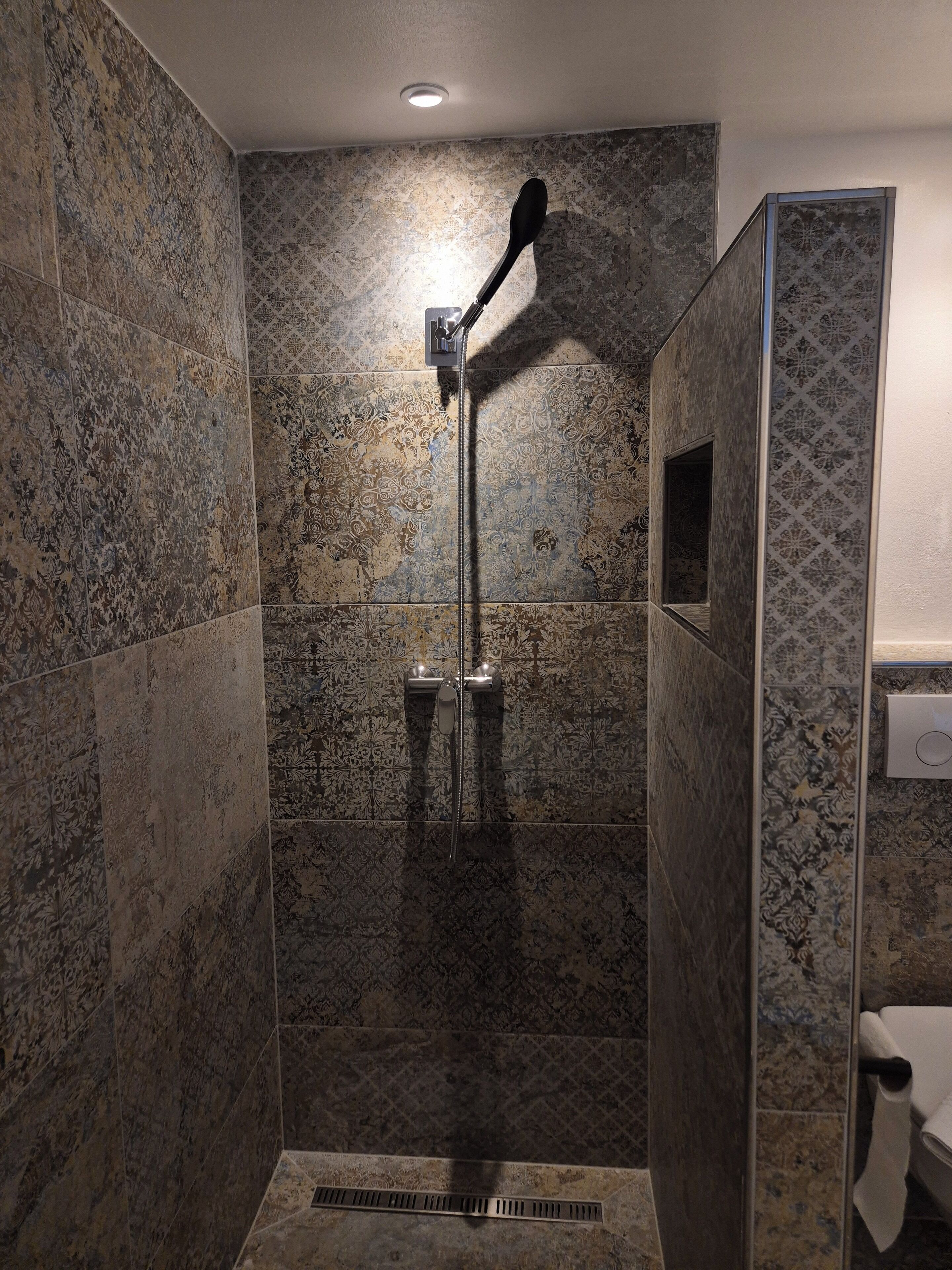 A shower with a handheld showerhead and a wall-mounted faucet.