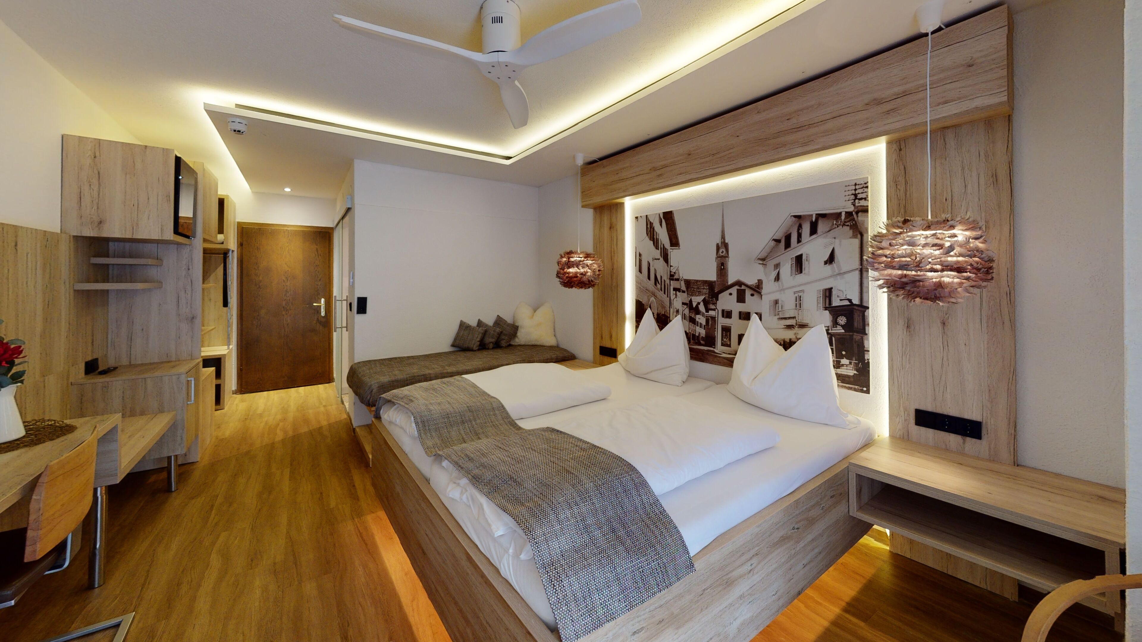 A modern bedroom with a large bed, built-in wooden shelving, and a cityscape mural on the wall.