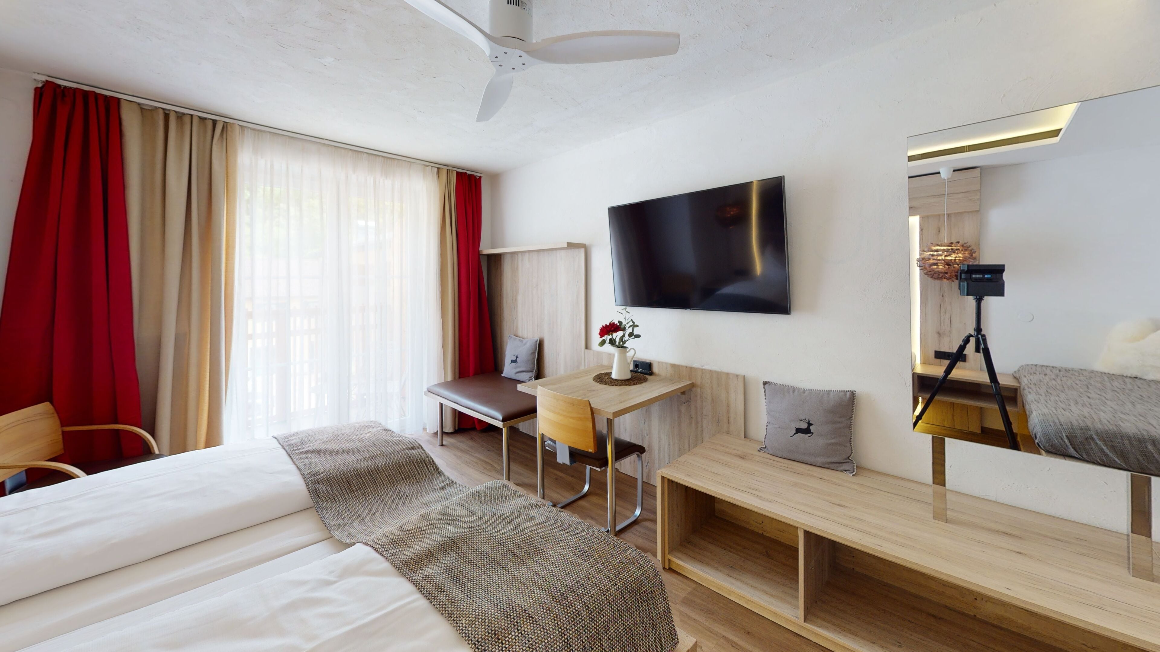 Une chambre d’hôtel moderne dotée d’un grand lit, d’un bureau avec une chaise, d’un téléviseur fixé au mur et d’un ventilateur de plafond.