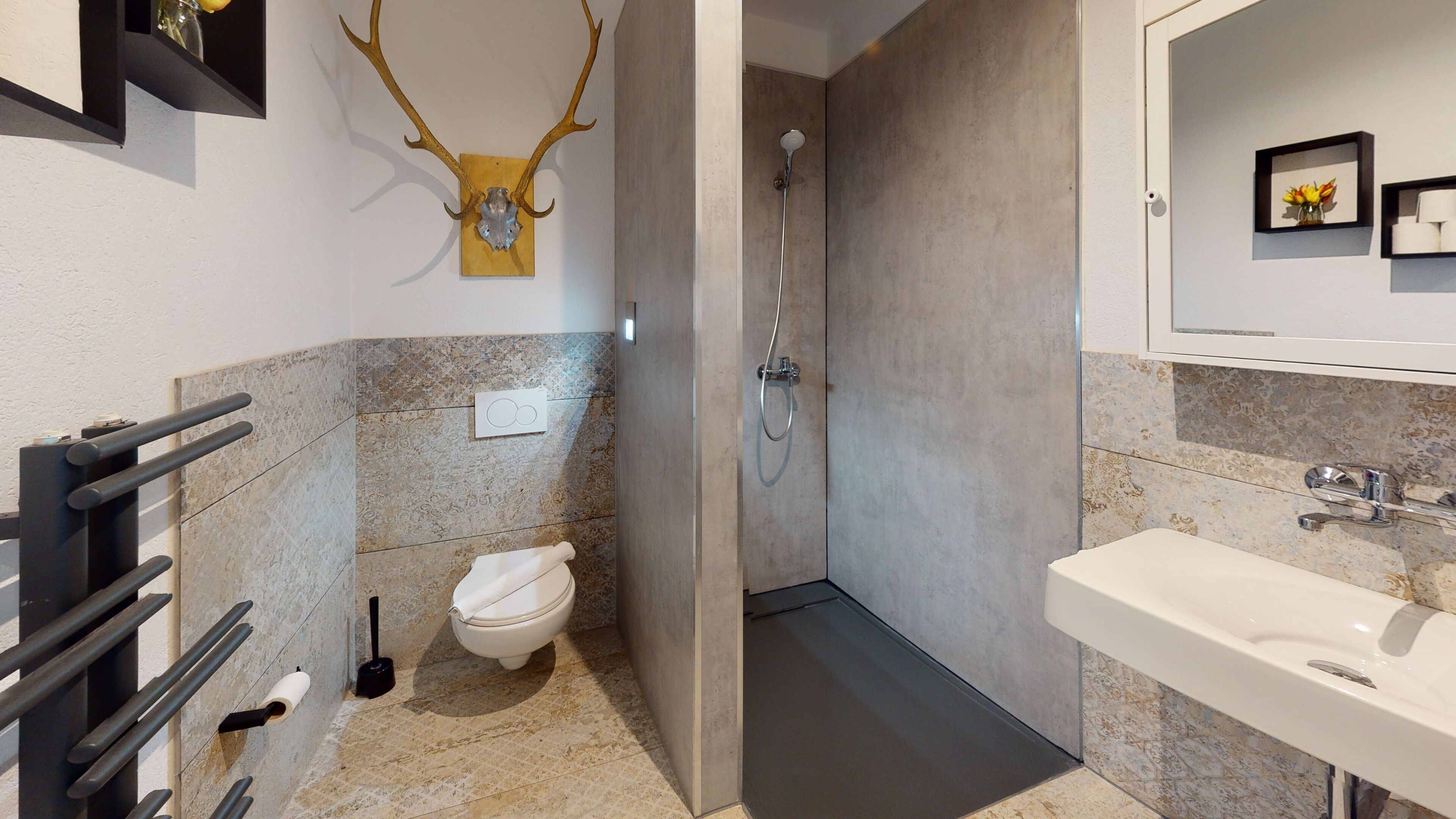 A bathroom with a toilet, shower, sink, and a deer skull decoration.