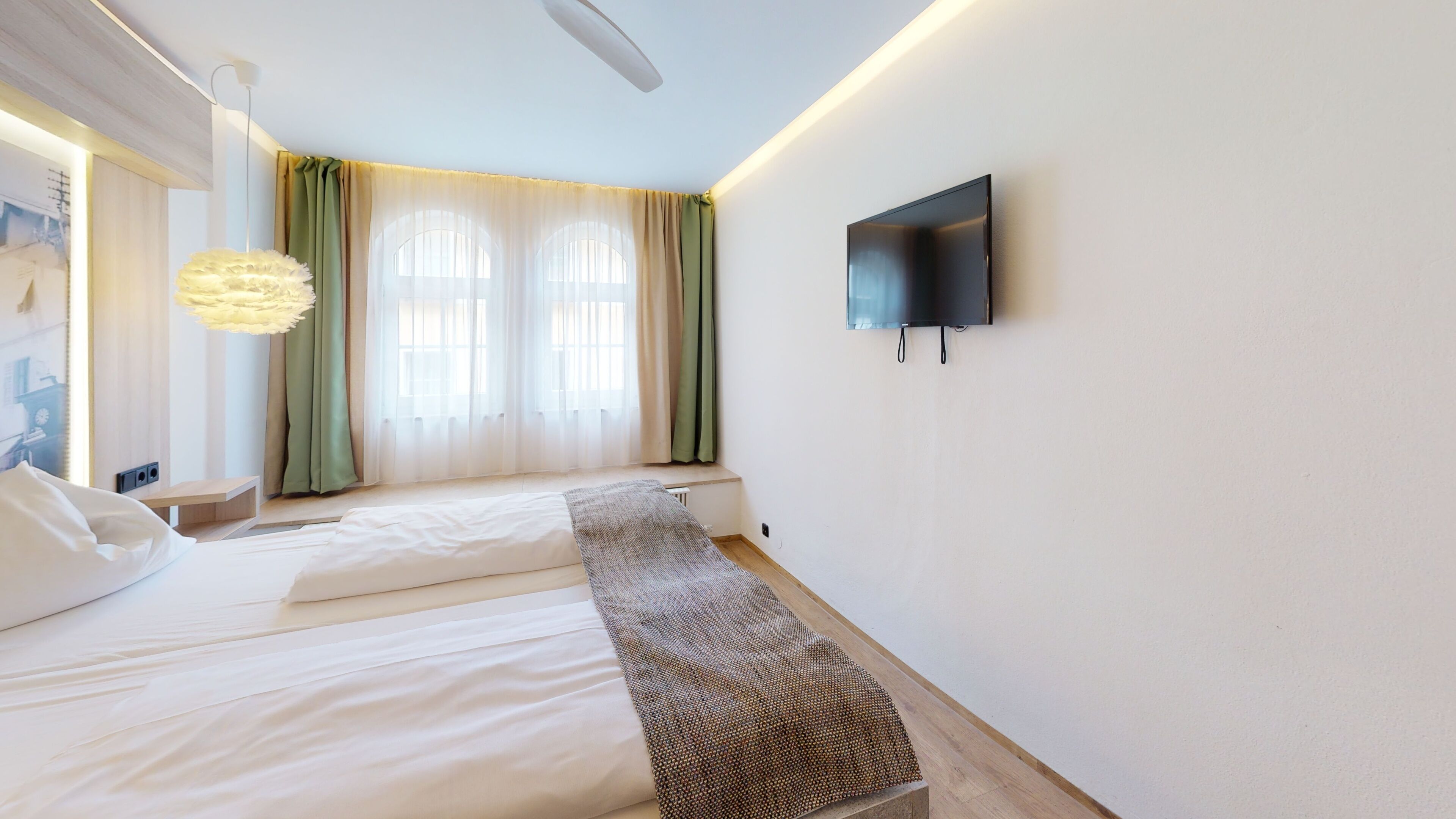Ein modernes Schlafzimmer mit Bett, einer Sitzbank, einem Fernseher und einem Fenster mit Vorhängen.