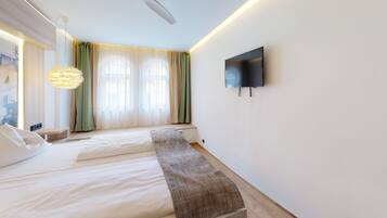 Ein modernes Schlafzimmer mit Bett, einer Sitzbank, einem Fernseher und einem Fenster mit Vorhängen.