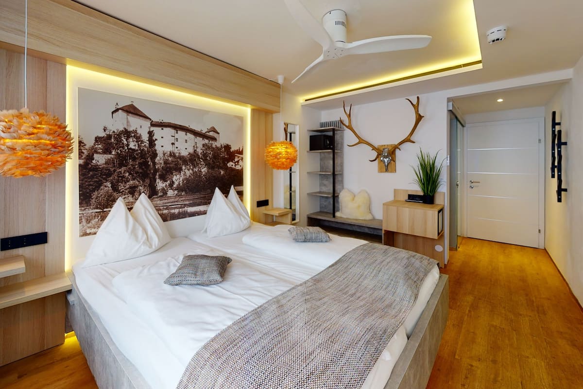 A modern bedroom with a large bed, a ceiling fan, a wall-mounted shelf, and a framed picture.