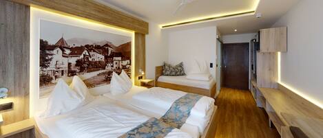 A modern hotel room with a large bed, a smaller bed, a desk, and a wooden headboard.