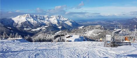 Eine verschneite Berglandschaft mit Seilbahn und Gebäuden im Vordergrund.