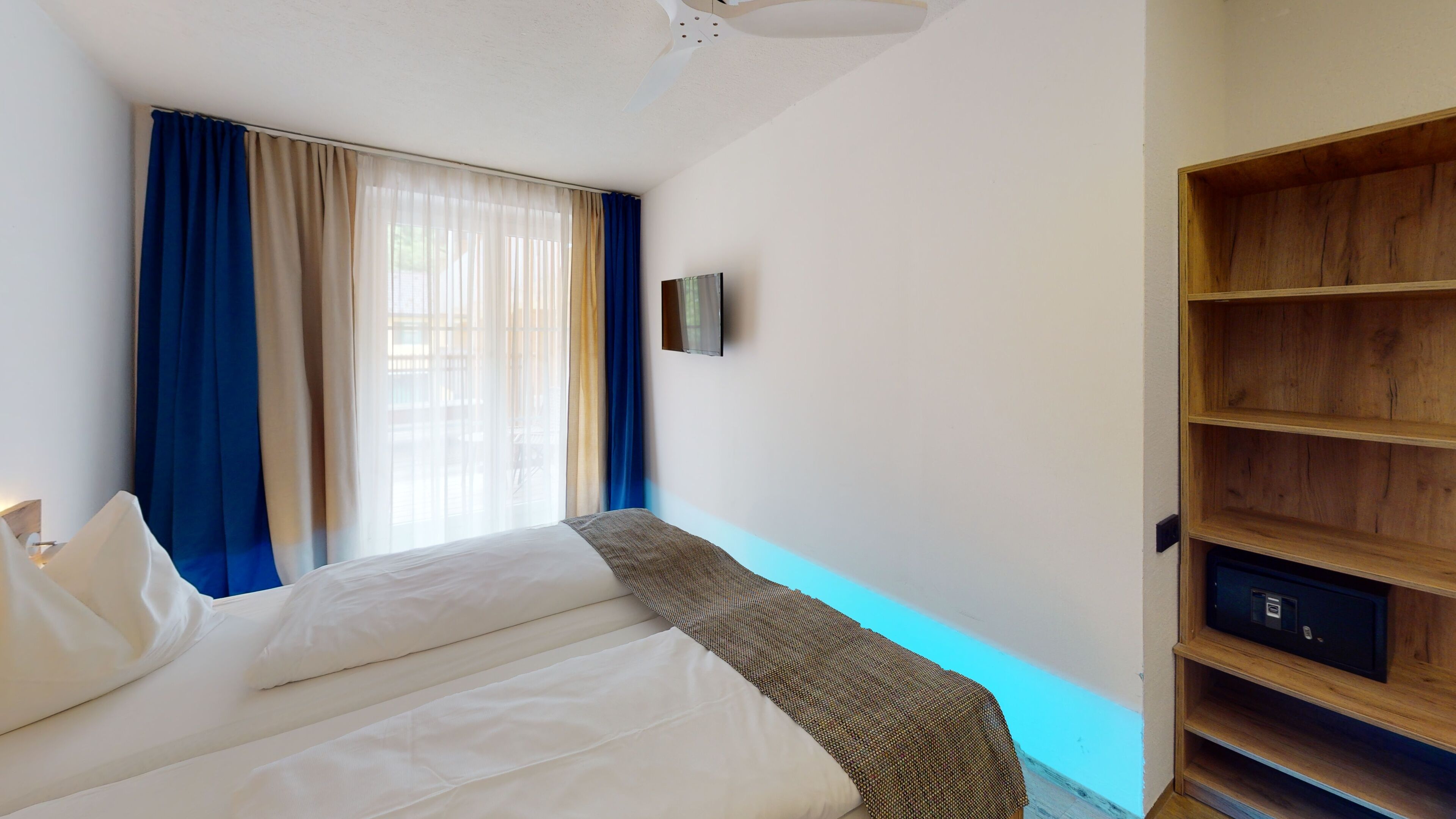 Ein Hotelzimmer mit einem Bett, einem an der Wand befestigten Fernseher und einer Holzregaleinheit.