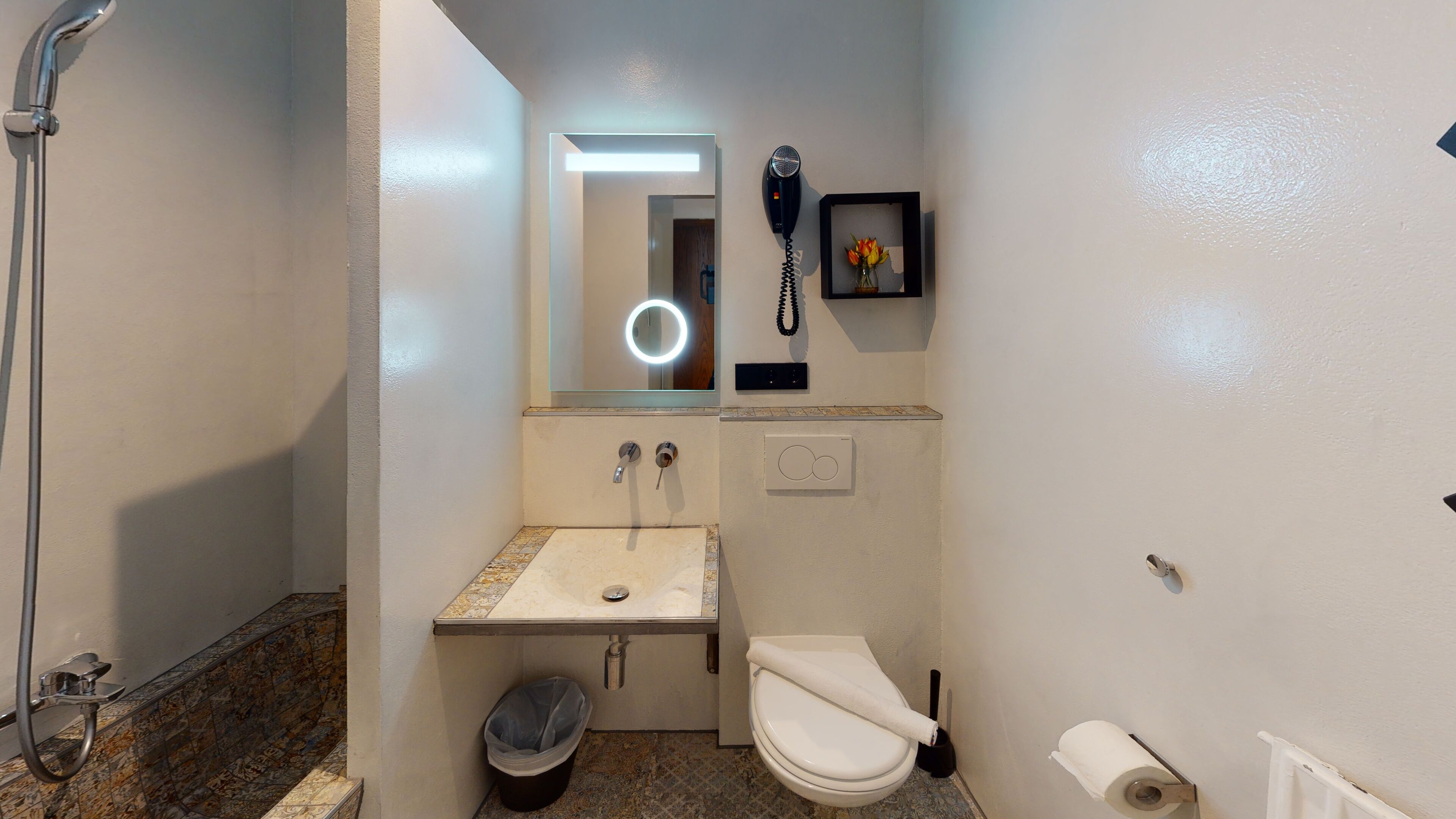 A compact bathroom with a shower, sink, toilet, and a hairdryer mounted on the wall.