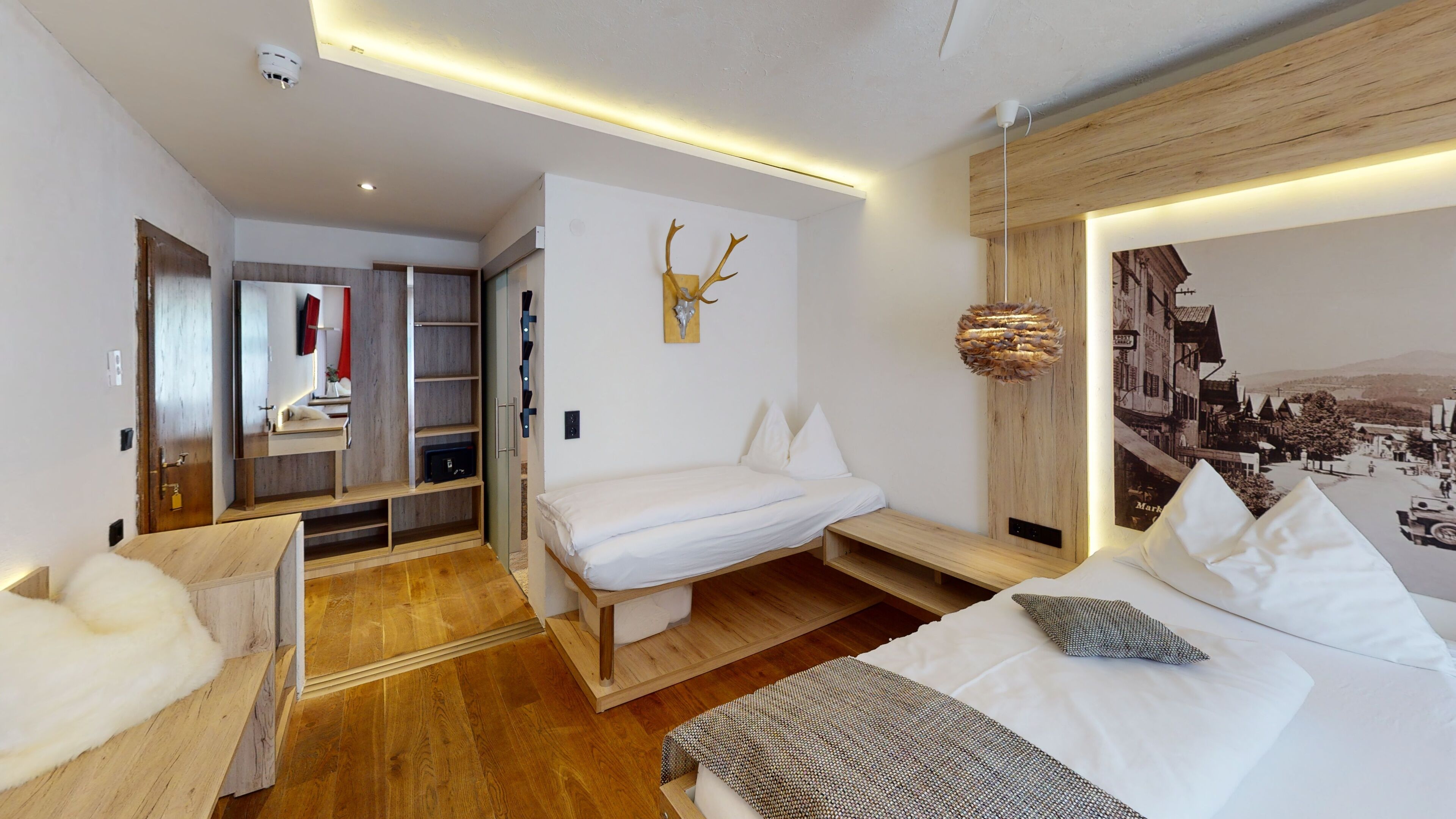 A modern hotel room with a bed, a small seating area, a wooden wardrobe, and a wall-mounted artwork.