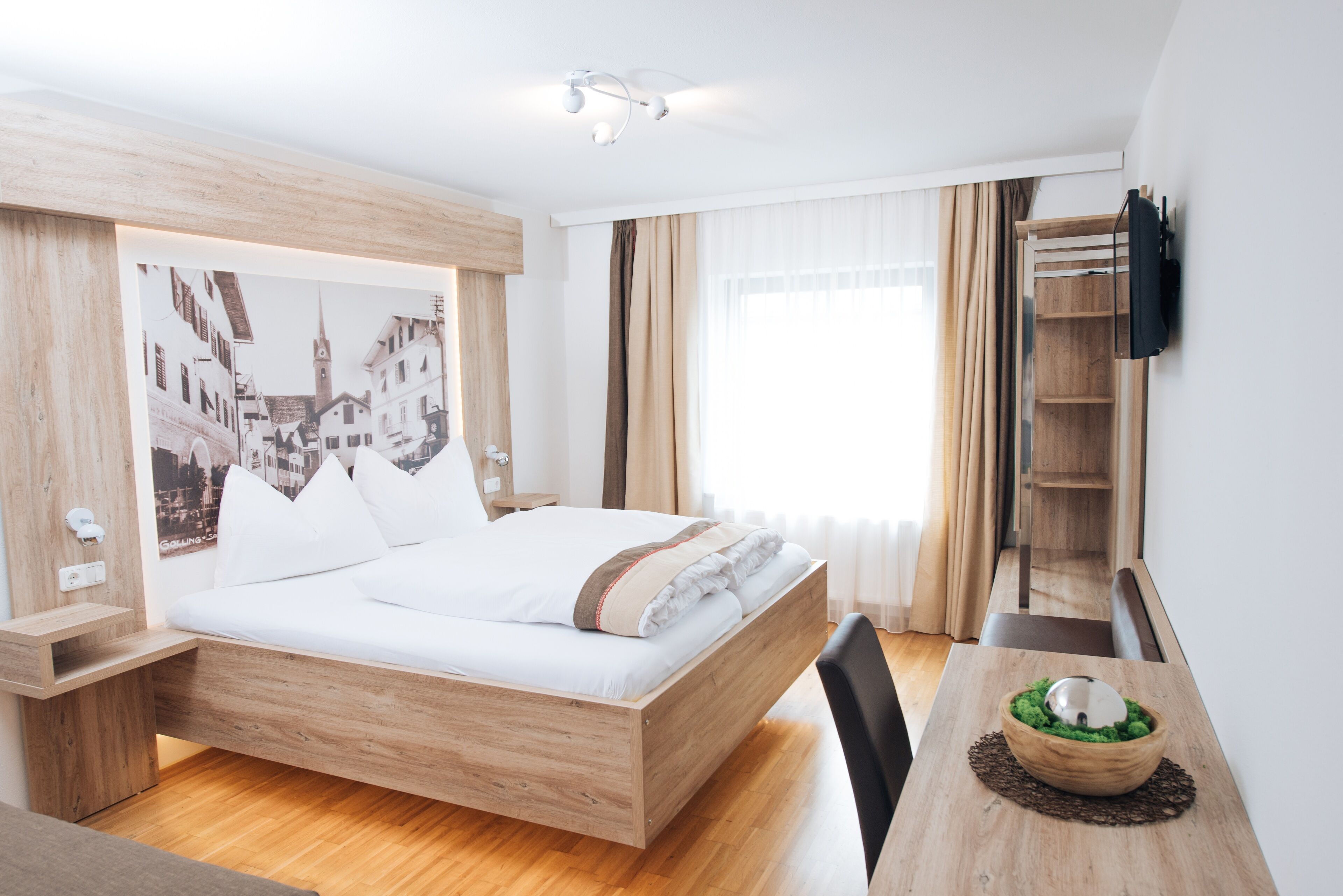 Et moderne hotelværelse med en træseng, et skrivebord med en skål og et fjernsyn monteret på væggen.