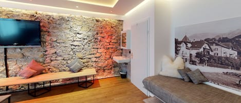A modern living room with a stone wall, a flat-screen TV, a sofa, and a large framed picture.
