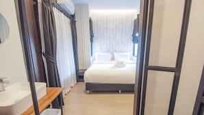 A modern hotel room with a large bed, a wooden bedside table, a white sink, and a window with curtains. - Sathu Hotel (Chiang Mai)