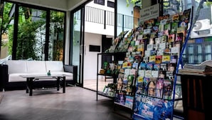 A modern interior with a white sofa, a coffee table, and a display of magazines and books. - Sathu Hotel (Chiang Mai)