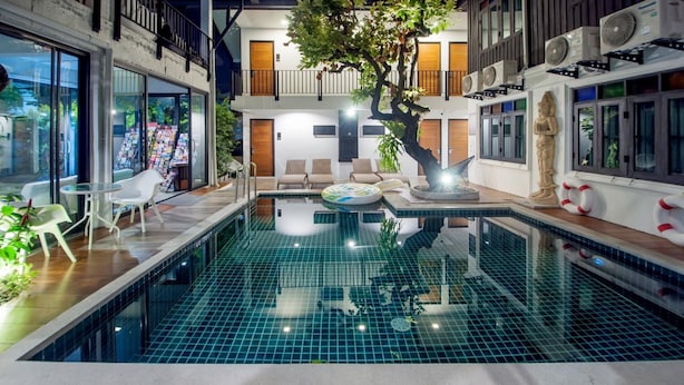 An indoor swimming pool with a tiled floor, surrounded by lounge chairs and a small table. - Sathu Hotel (Chiang Mai)