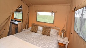 Una tienda de campaña con una cama, una ventana y una pequeña mesa con un farol.