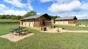 Dos cabañas rústicas con terrazas de madera y mesas de picnic en un campo cubierto de hierba.