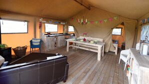 Alojamiento con carpa, zona de comedor, sofá, mesa para dos y kitchenette.