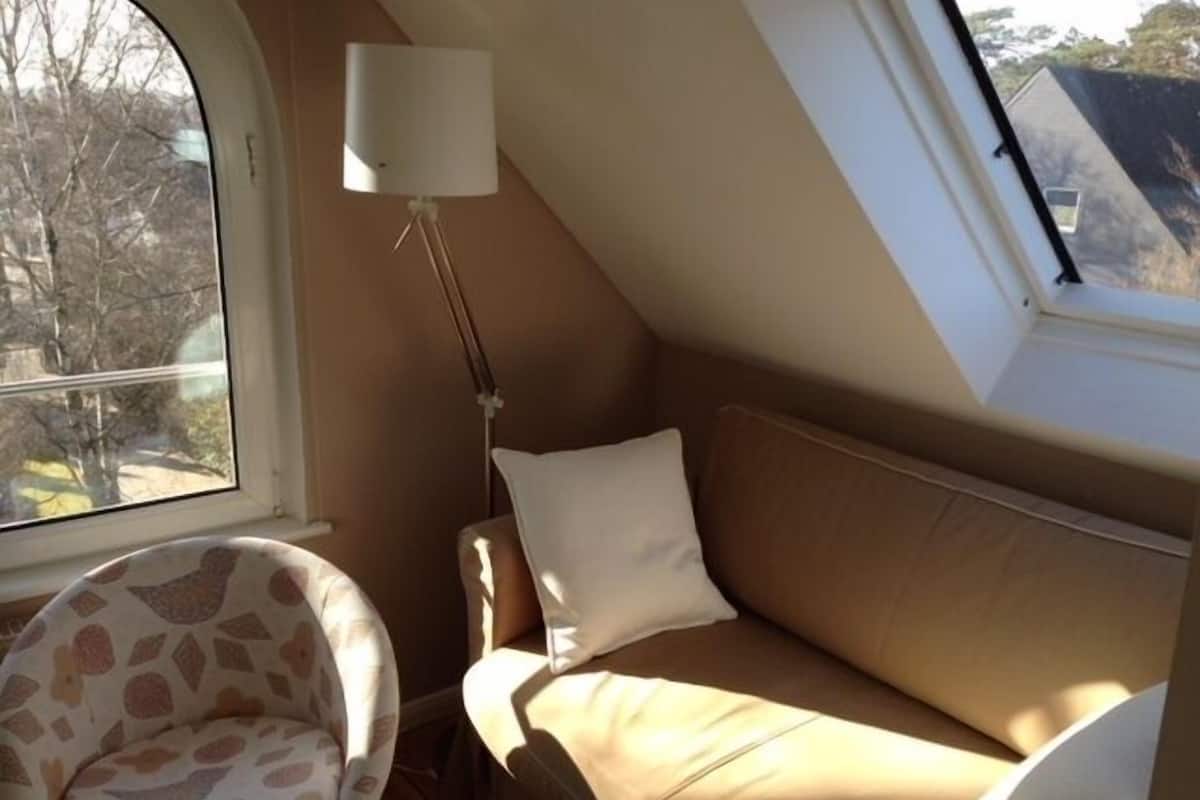 A cozy room with a sloped ceiling, a window, a sofa, a chair, and a floor lamp.