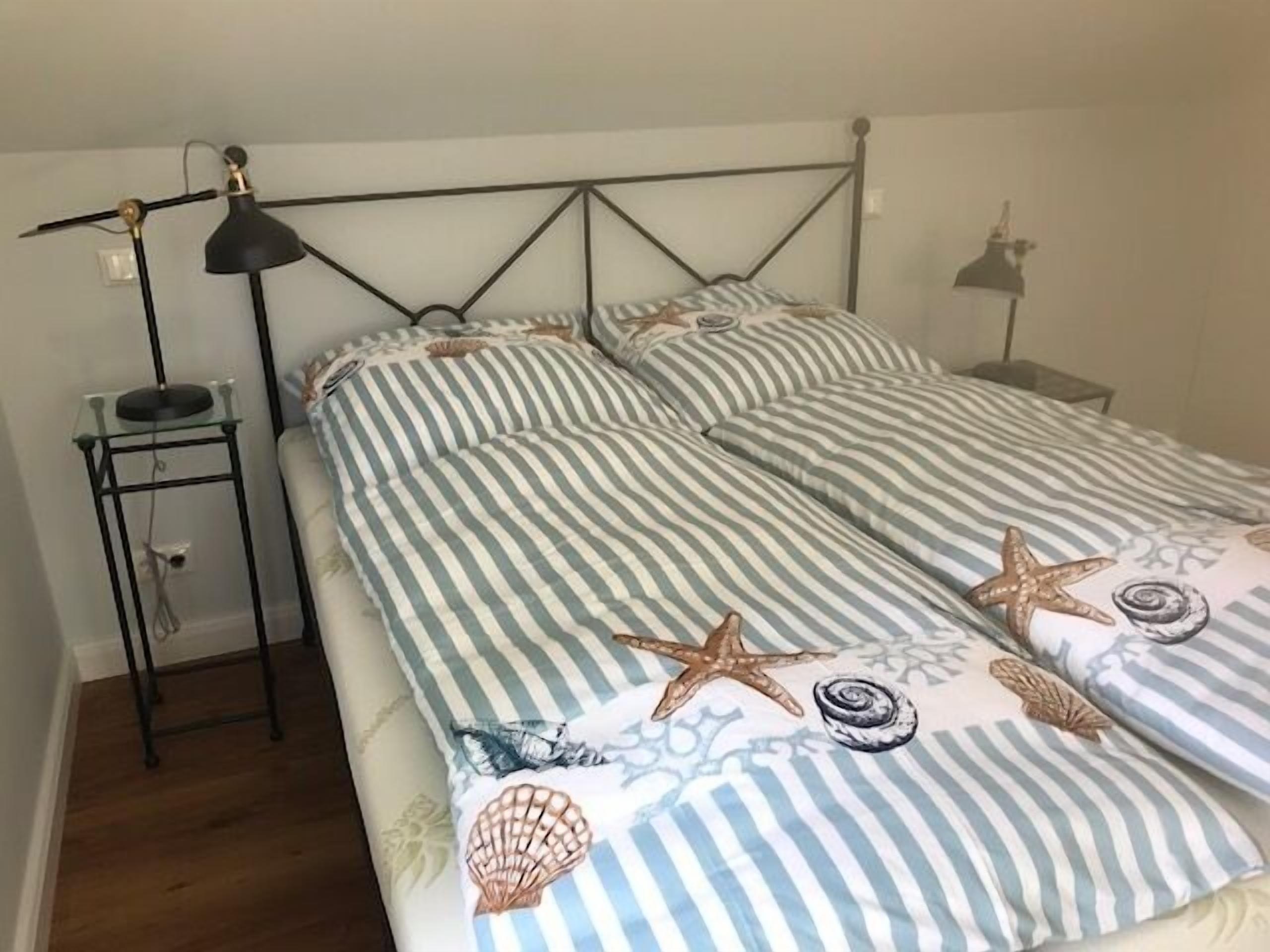A bed with striped bedding and starfish designs, a bedside table with a lamp, and a small shelf unit.