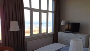 A hotel room with a bed, a TV, a dresser, and a window with a view of the beach. - Kleines Strandhotel (Timmendorfer Strand)