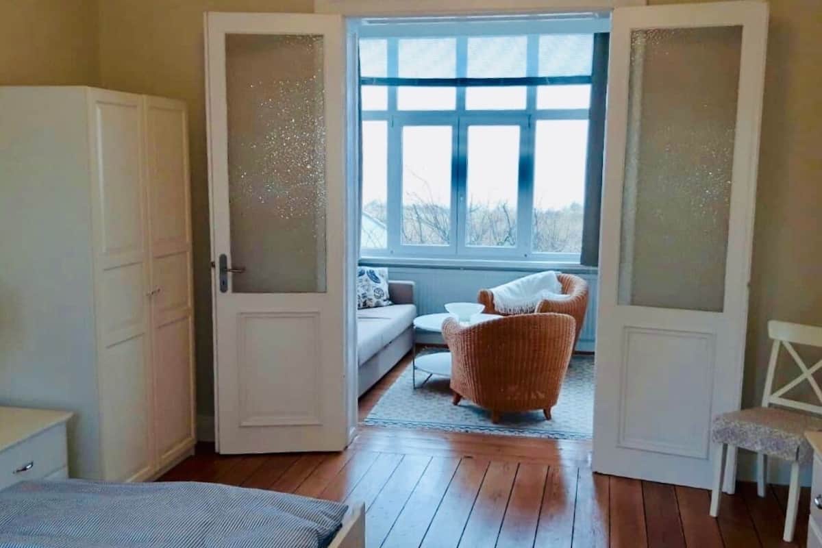 A bedroom with a bed, a chair, a sofa, and a window with a view of trees.