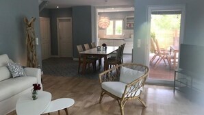 A spacious living area with a sofa, a white coffee table, and a wicker chair. There is a dining table with chairs in the background. - Kleines Strandhotel (Timmendorfer Strand)