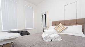 A hotel room with a large bed, a grey fluffy blanket, a neatly folded white towel, and a striped pillow. - Kirkstall House (Leeds)