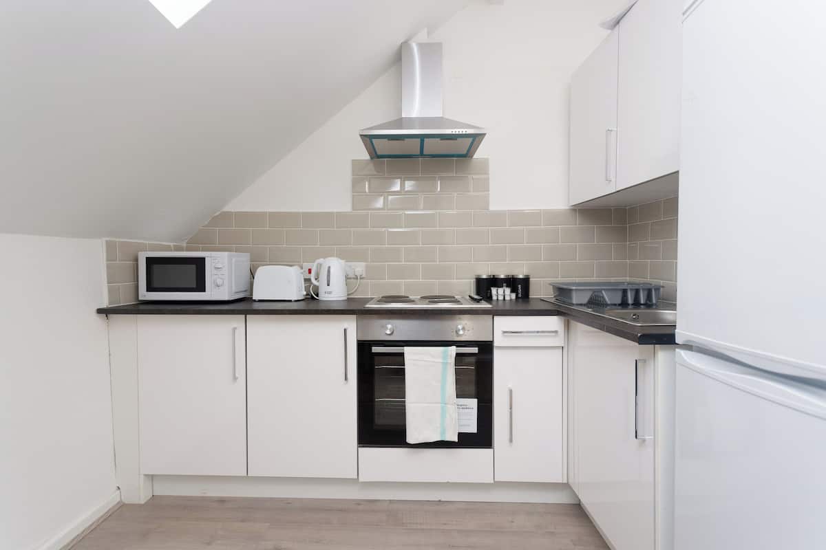 A compact kitchen with white cabinets, a microwave, a kettle, a toaster, a stove, and a dishwasher.