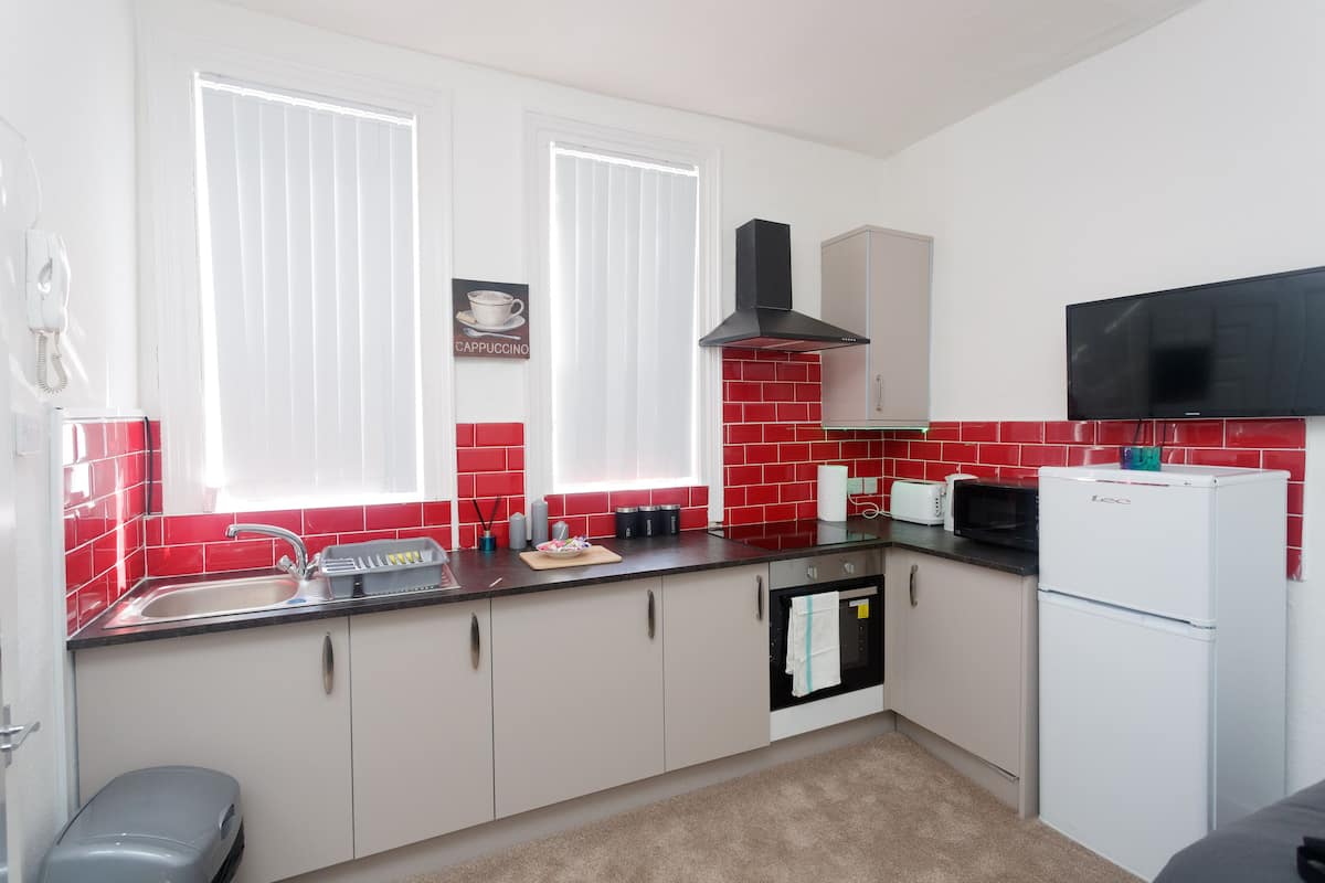 A compact kitchen with white cabinets, a black countertop, a microwave, a toaster, and a refrigerator.