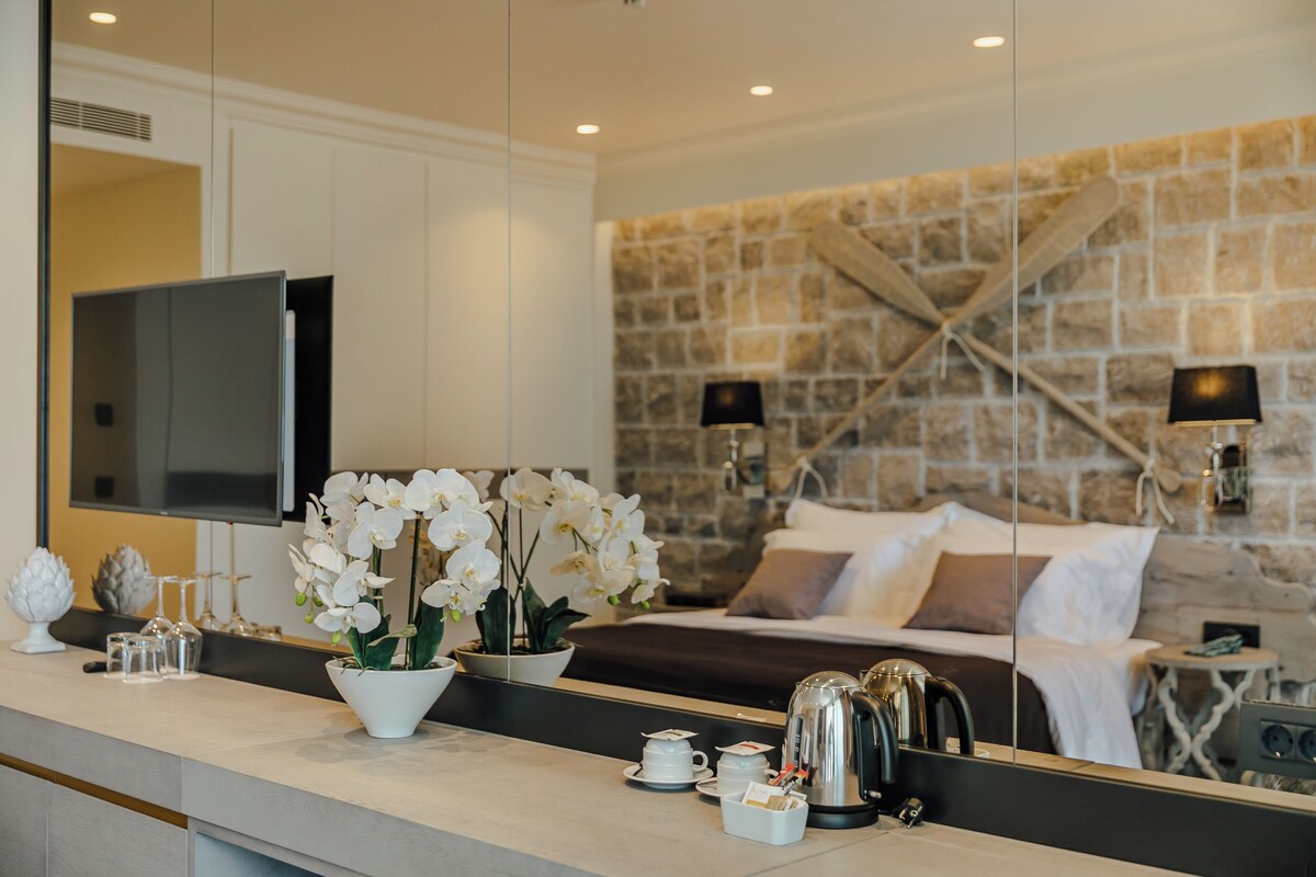 A hotel room with a stone wall, a bed with white bedding, a coffee maker, and a TV on the wall.