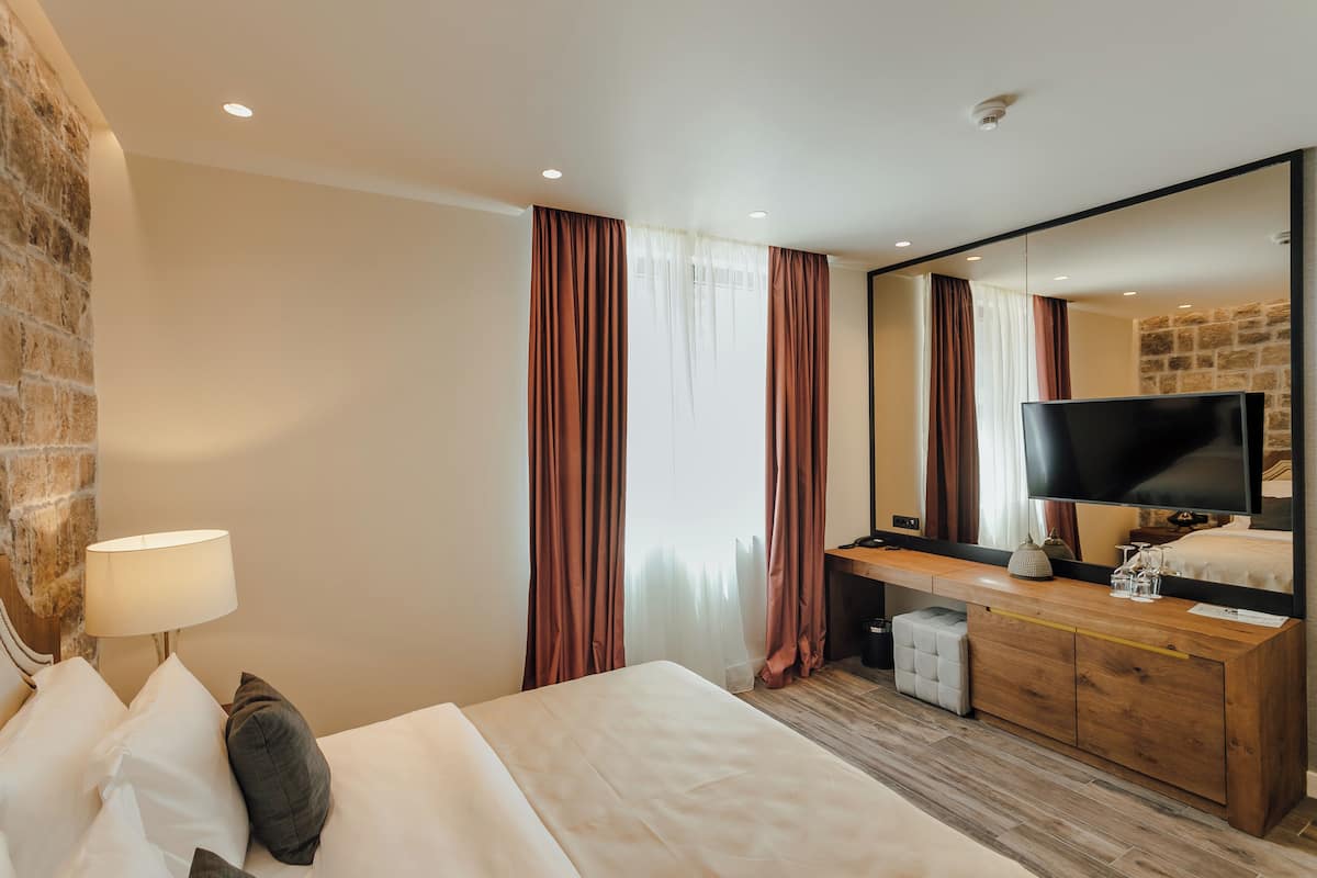 Una habitación de hotel con una cama, un aparador de madera, un televisor y un espejo grande.