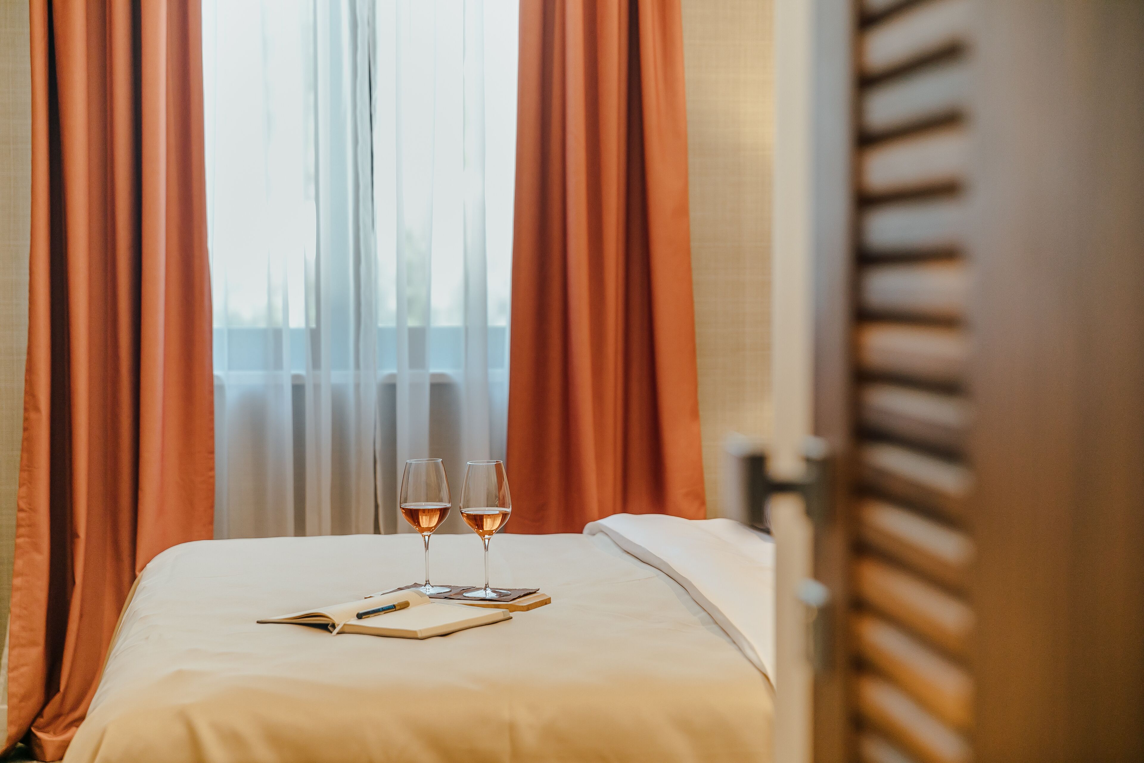 A neatly made bed with two wine glasses and a notebook on it.