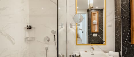 Un baño moderno con ducha de vidrio, un lavabo blanco con encimera negra y un espejo grande con marco dorado.