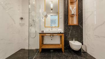 A modern bathroom with a glass-enclosed shower, a wooden vanity, a bidet, and a marble-tiled floor.