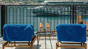 Deux chaises bleues, chacune avec une serviette, une petite table avec deux boissons, et une vue sur un navire de croisière et l’eau.