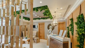 Un espace d’accueil avec un comptoir de réception en bois, un grand miroir et une plante suspendue.