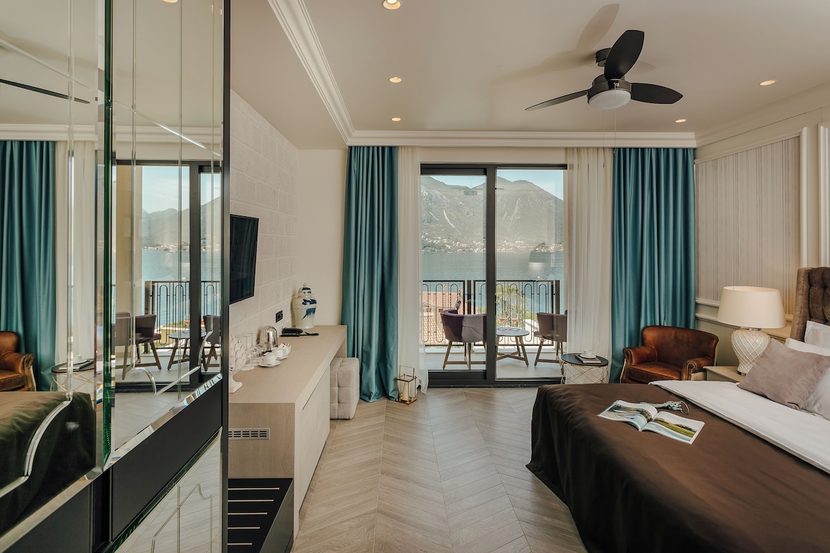 Habitación de hotel con cama, escritorio, silla, sofá, balcón y vistas a las montañas, además de un ventilador de techo.