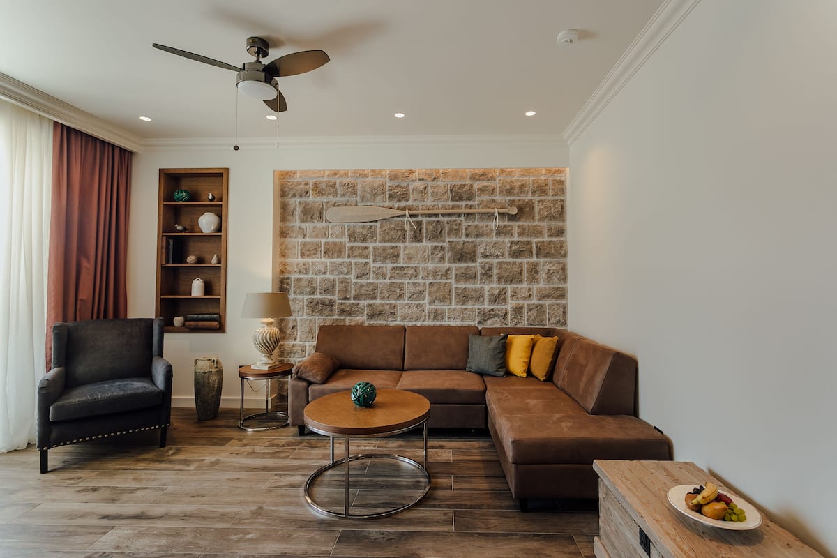 Un salón moderno con un sofá de cuero marrón, una mesa de centro redonda, un sillón negro y una pared de piedra.